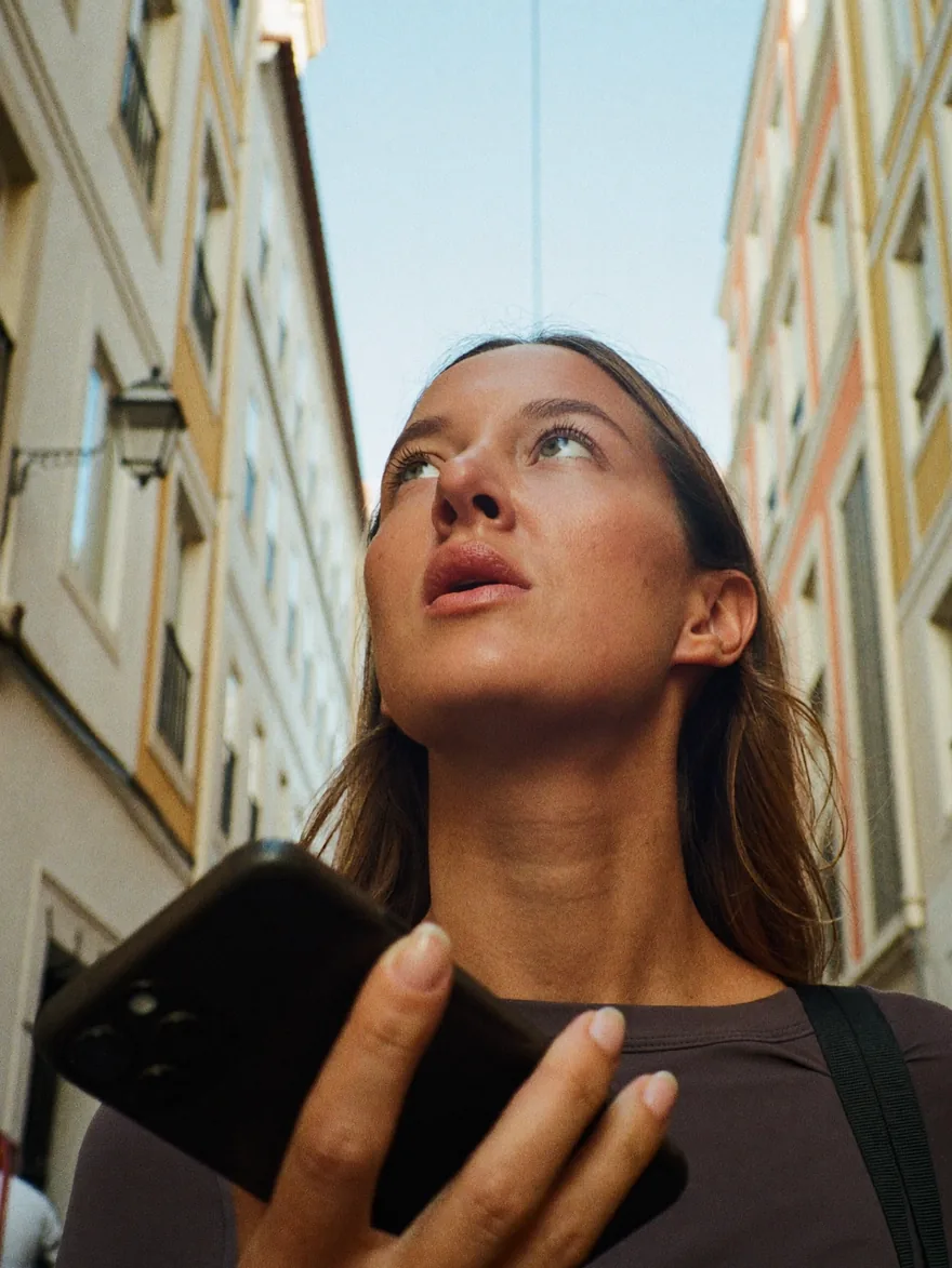 A traveler in a narrow old-town street looks up from the phone in her hand